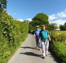 Randall and Mike stride along a narrow Lakeland road